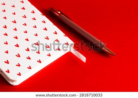 Macro shot of a section of a white notebook with a heart pattern and a premium pen, capturing the paper texture on a flat red background.