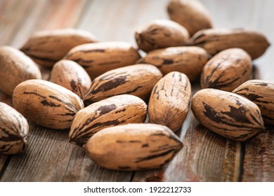 A macro shot with selective focus of a handful of pecan nuts in shells set on a wood table.