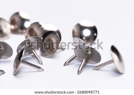 A macro shot of several silver thumb tacks scattered on a white surface, highlighting their shiny metal texture and sharp points.
