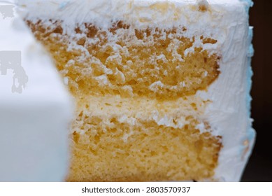 A macro shot showing a cross-section slice of a fluffy sponge cake layered with sweet cream filling and covered in thick white icing.
