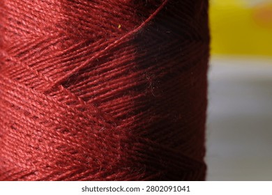 Macro shot of a spool of dark red sewing thread showing detailed fiber texture.