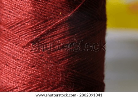 Macro shot of a spool of dark red sewing thread showing detailed fiber texture.