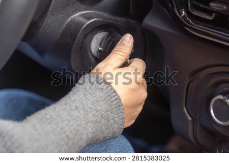 Macro shot of thumb touching ignition switch marked lock acc on, dashboard and air vent visible, car interior detail