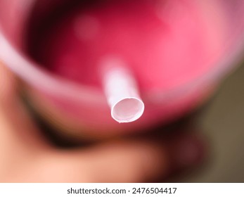 A macro shot of the top of a straw inserted into a cup of pink beverage. The cup is held in a hand in the blurred background.