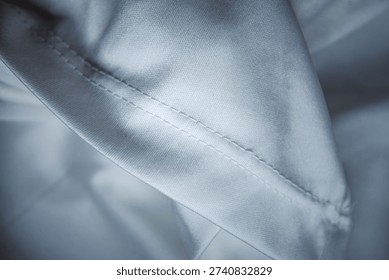 Macro shot of white technical fabric featuring a professional double stitched seam. High-quality smooth textile background with soft folds for apparel manufacturing and fashion design.