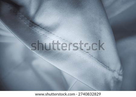 Macro shot of white technical fabric featuring a professional double stitched seam. High-quality smooth textile background with soft folds for apparel manufacturing and fashion design.