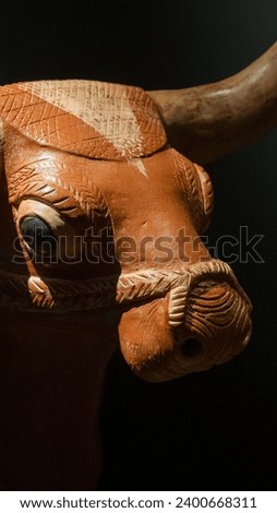 A macro shot of a wooden sculpture of a bull head from the bronze age on a black background.