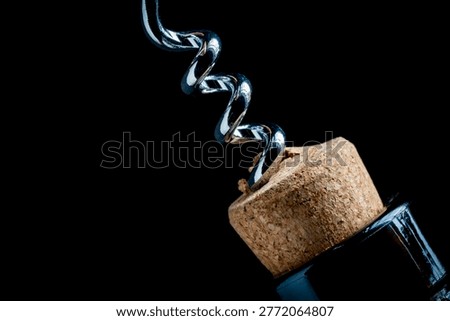 Macro of silver corkscrew opening wine bottle with cork. Close up of a metal corkscrew twisting into a wine cork. Concept of opening a bottle celebration and winery service on a dark background