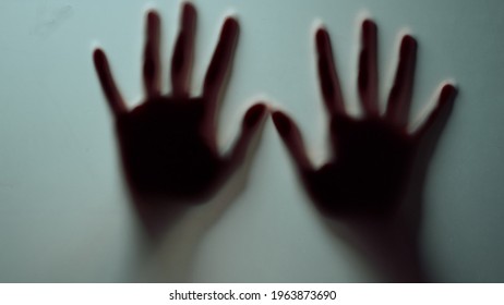 Macro Of Two Female Hands Pressing Against Glass Wall Indoors. Abstract Defocused Fists Sliding On Frosty Glass. Horror Video Blurred Silhouette Hands Shadow Disappearing Magically In Smoggy Studio.