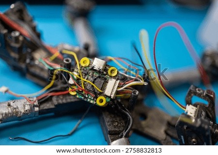 Macro view of a 5-inch FPV drone flight controller during disassembly and repair, highlighting exposed wiring, onboard components, and technical detail on a blue electronics workbench.