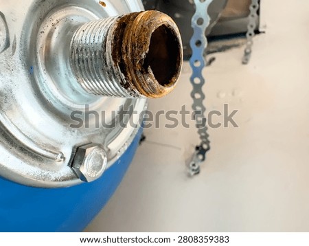 Macro view of a corroded threaded connector on a blue expansion vessel from a home water heating system. Rust on the pipe thread that caused a water leak.