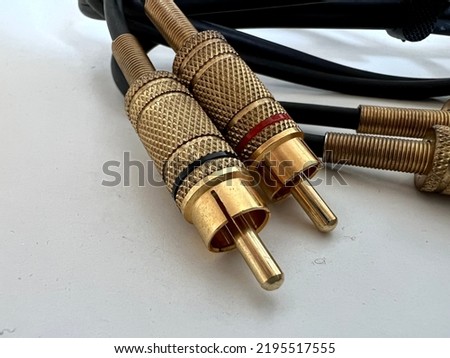Macro view gold-plated phono connectors at end of black audio cable, resting on plain white surface