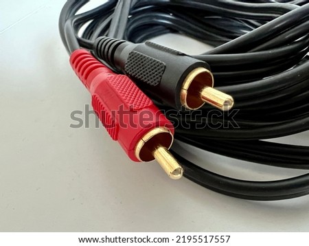 Macro view gold-plated phono connectors with red and black plastic covers, at end of black audio cable, resting on plain white surface