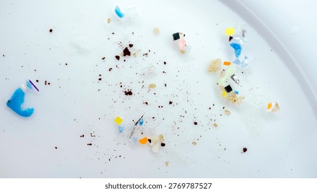 Macro view of microplastic pieces scattered on a Petri dish. A collection of plastic fragments and sediment highlights the global ocean pollution. Micro plastic particles and synthetic debris
