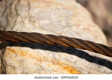 Macro View On An Old And Rusty Steel Cable Above A White Rock