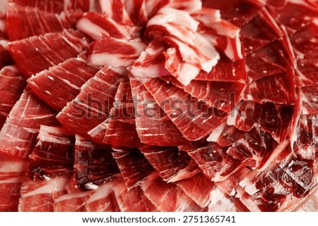 A macro view of premium cured jamon serrano slices arranged in a circular pattern showing rich red meat and fat.
