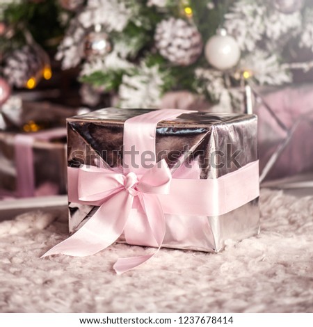 Macro view of present christmas box with tender pink ribbon. gift under the eve tree