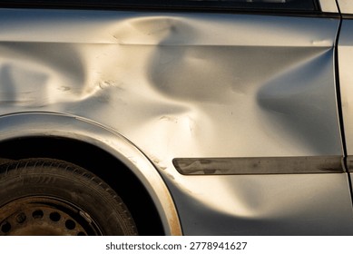 Macro view of a silver car surface showing a large impact dent and scratched paint after a vehicle accident or collision