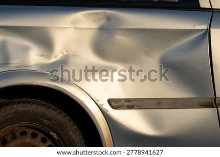 Macro view of a silver car surface showing a large impact dent and scratched paint after a vehicle accident or collision