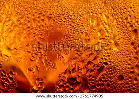 Macro view of the surface of a cola drink; a close-up image of a refreshing iced tea with water droplets clinging to the glass,Macro shot of a cold amber beverage, likely iced tea or soda, showing detailed water droplets and condensation on the outside of a chilled glass, symbolizing refreshment, thirst, and summer heat.