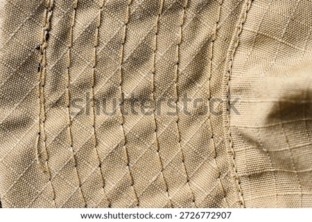 Macro view of tan ripstop textile showing detailed weave and multiple parallel rows of heavy-duty reinforced stitching, ideal for tactical, military, or industrial fabric backgrounds