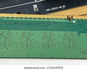 Macro view of two computer RAM modules with gold contact pins. Detailed shot of a green printed circuit board (PCB) showing intricate copper traces and solder points placed on top of another black electronic component.