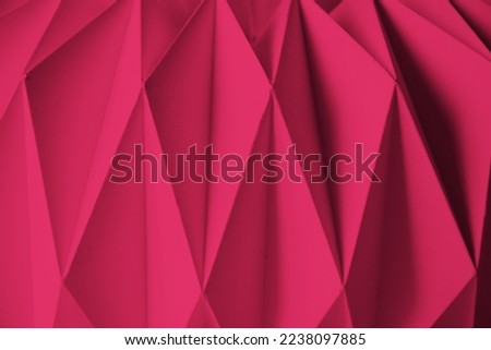 Macro Viva Magenta image of paper folded in geometric shapes, three-dimensional effect, abstract background. Out of focus. Trendy color 2023 Viva Magenta.