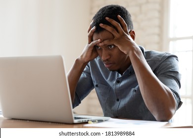 Mad African American young male employee look at laptop screen having operational software problems, angry biracial man worker work in office annoyed with slow Internet connection on computer