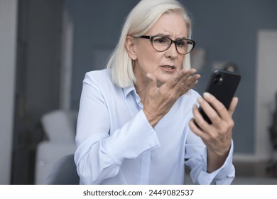 Mad businesswoman sits at workplace gawp at smartphone screen, experiencing technical issues, app crash, touchscreen malfunction, connectivity issues, battery is draining rapidly, receive scam message - Powered by Shutterstock