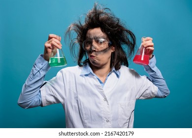 Mad Chemist Having Beakers Filled With Toxic Liquid Substances While On Blue Background. Goofy Looking Wacky Scientist Holding Professional Glass Jars Filled With Toxic Chemical Compounds. Studio Shot