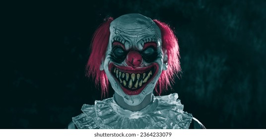 a mad evil redhead clown, wearing a white and red striped costume with a white ruff, stands with closed eyes and a creepy smile on a dark background, in a panoramic format to use as web banner