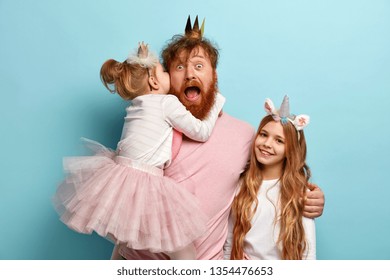 Mad father hears secret from daughter, spends free time with children, embraces and shares love, wear carnival costumes for party, isolated over blue wall. Kids and parents concept. Festive event - Powered by Shutterstock