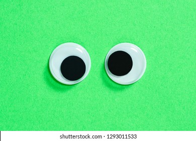 Mad googly eyes on neon green background, cross-eyed funny toys eyes close-up. - Shutterstock ID 1293011533
