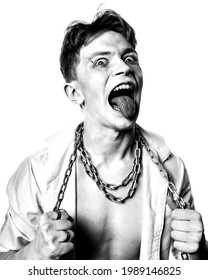 A mad lunatic with makeup and a chain wrapped around his neck screams against a white background. Black and white contrast portrait.