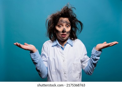 Mad Scientist With Funny Expression And Wacky Hair, Shrugging Shoulders While On Blue Background. Silly Looking Crazy Foolish Chemist With Dirty Face Lifting Shoulders With Ignorance. Studio Shot.