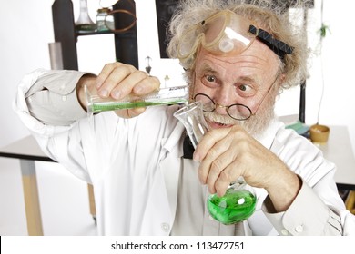 Mad Senior Scientist In Lab Concentrates On Pouring Green Liquid Into Beaker. Frizzy Grey Hair, Round Glasses, Lab Coat, Blackboard, Vertical, High Key, Copy Space.