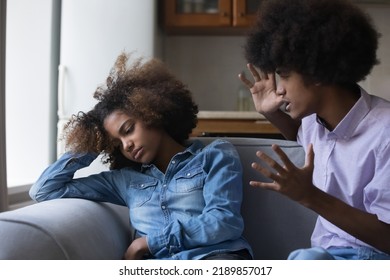 Mad Teenage African Guy Screams At Girlfriend During Quarrelling Seated On Sofa At Home. Jealousy, Bad Toxic Relations Of Young Couple, Fight, Moral Pressure And Control In Relationship, Abuse