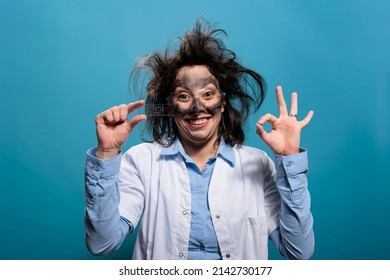 Mad Wacky Scientist With Glass Microscope Slide Looking Confused After Dangerous Lab Explosion. Insane And Pleased Biochemistry Specialist Looking Messy, Doing Good Job Gesture With Hand. Studio Shot.