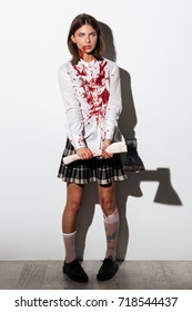 Mad woman in zombie make up covered with blood stains standing and holding an axe isolated over white background