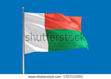 Madagascar national flag waving in the wind on a deep blue sky. High quality fabric. International relations concept.