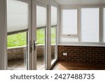 Made to measure blinds on windows and doors in a white conservatory with wooden floor and red brick walls on a sunny day. The roof is an insulated warm roof with mock beams.