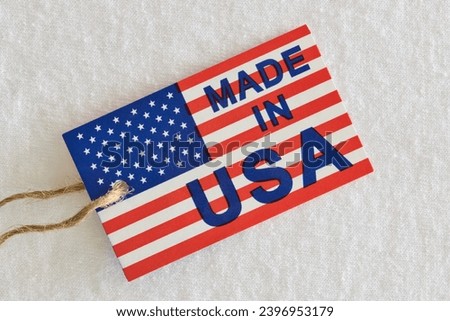 Made in USA label sitting on top of white clothing as a business economics concept. Flat lay macro image with patriotic background details.