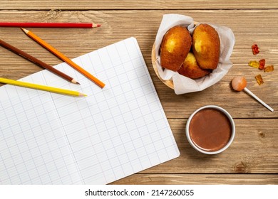 Madeleine cookie or French sponge cake alongside a blank school book, coloring pencils, lollypop, candies and hot chocolate on wood background with copy space, reference to the Marcel Proust, Flat lay
