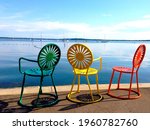 Madison, WI, USA. Three colorful chairs overlook sailboats moored on lake Mendoza at the Memorial Union Terrace.