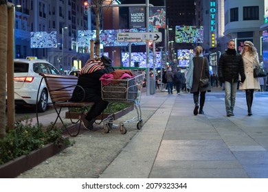 Madrid, Spain; 1 1 2020: Night view of a homeless man sitting with his cart of clothes at Christmas on Gran Via in Madrid Spain