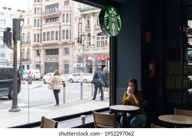MADRID, SPAIN - APRIL 08, 2021: Young Woman Drinking Coffee At A Table Inside The Starbucks In Madrid In Spain
