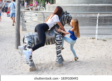 Madrid, Spain, August 21, 2019 - Two Sisters Playing On A Wooden Big Zebra At The Madrid Zoo. The Family Has Fun In The Fresh Air.