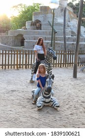 Madrid, Spain, August 21, 2019 - Two Sisters Playing On A Wooden Big Zebra At The Madrid Zoo. The Family Has Fun In The Fresh Air.