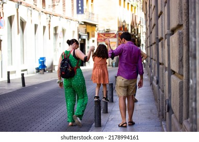 Madrid, Spain. July 2, 2022. Happy Family - Mom, Dad, Little Girl Daughter Walking Down City European Street. People Are Walking In Summer Holidays, Travel Together. Kid Jumping. Parenthood Childhood.