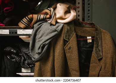 Madrid, Spain. May 1, 2022 An Old Brown Wool Jacket Hangs On A Rack In A Secondhand Clothing Warehouse. Humanitarian Aid Distribution Point For Refugees, Homeless, Destitute. Warm Clothes On The Shelf